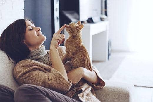 Femme assise sur une chaise tenant un chat roux tigré et lui touchant doucement le nez